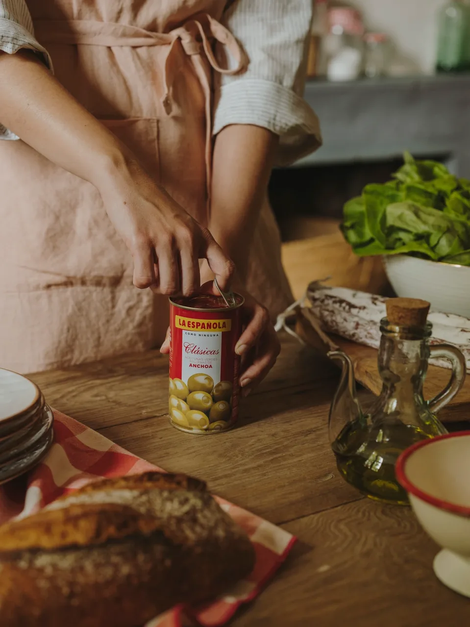 Hands opening a La Española anchovy-stuffed olive tin in a rustic kitchen