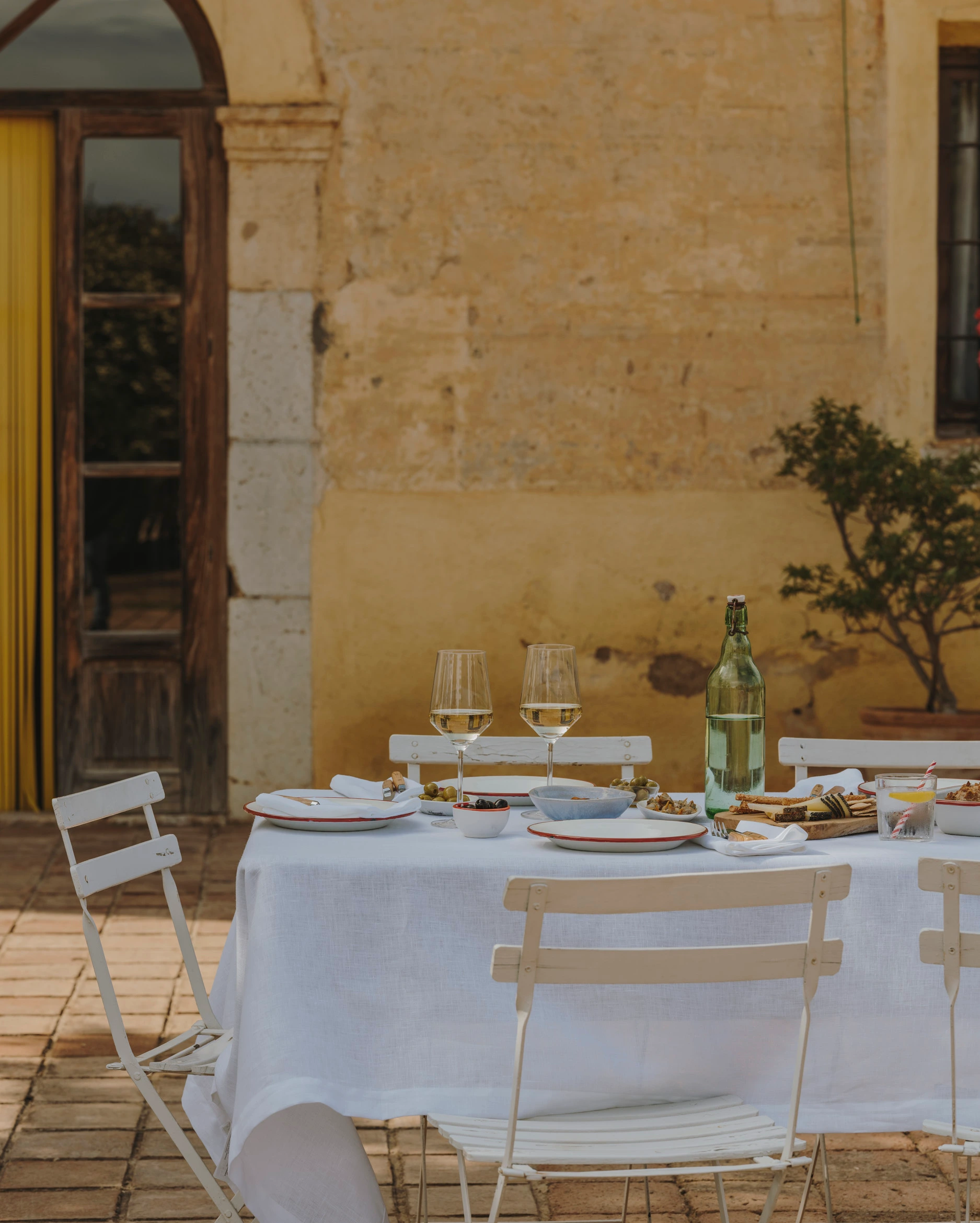 Outdoor courtyard table set for lunch, white linens, ochre wall
