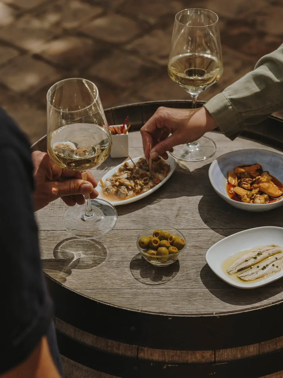 Two people sharing tapas and white wine on a wine barrel table